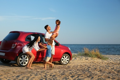 Photo of Happy family having fun near car on sandy beach. Summer trip