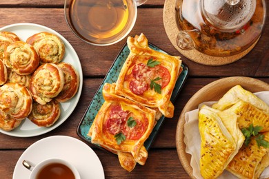 Various delicious puff pastry served with tea on wooden table, flat lay