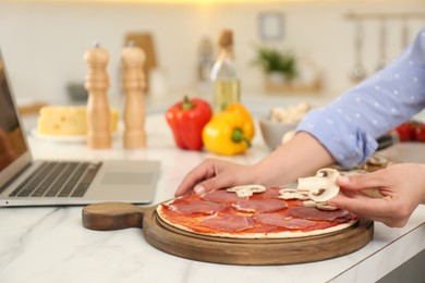 Photo of Woman making pizza while watching online cooking course via laptop in kitchen, closeup