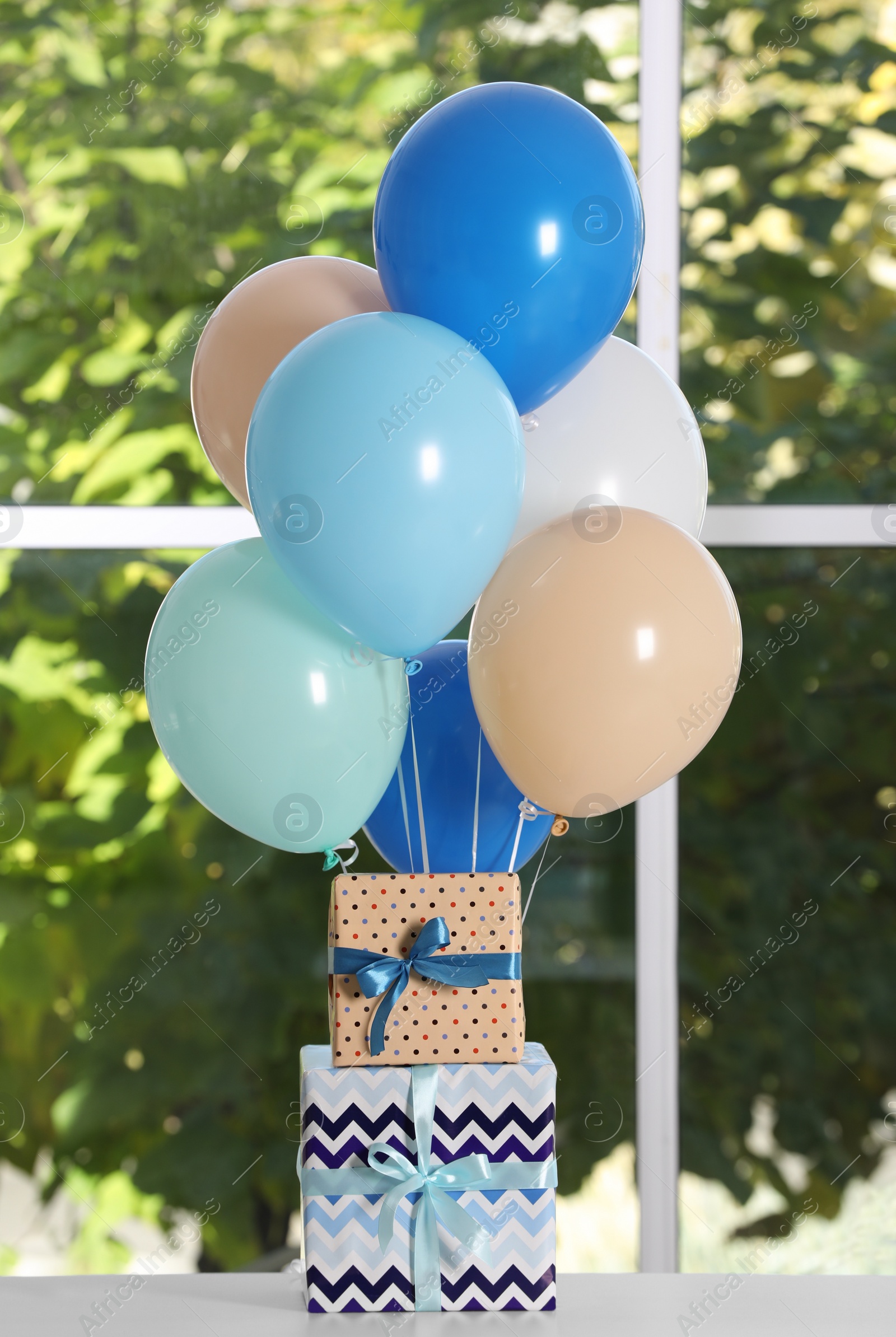 Photo of Bunch of color balloons and beautifully wrapped gift boxes on white table near window