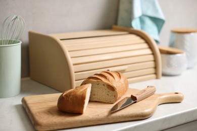 Photo of Wooden bread basket, freshly baked loaf on white marble table in kitchen
