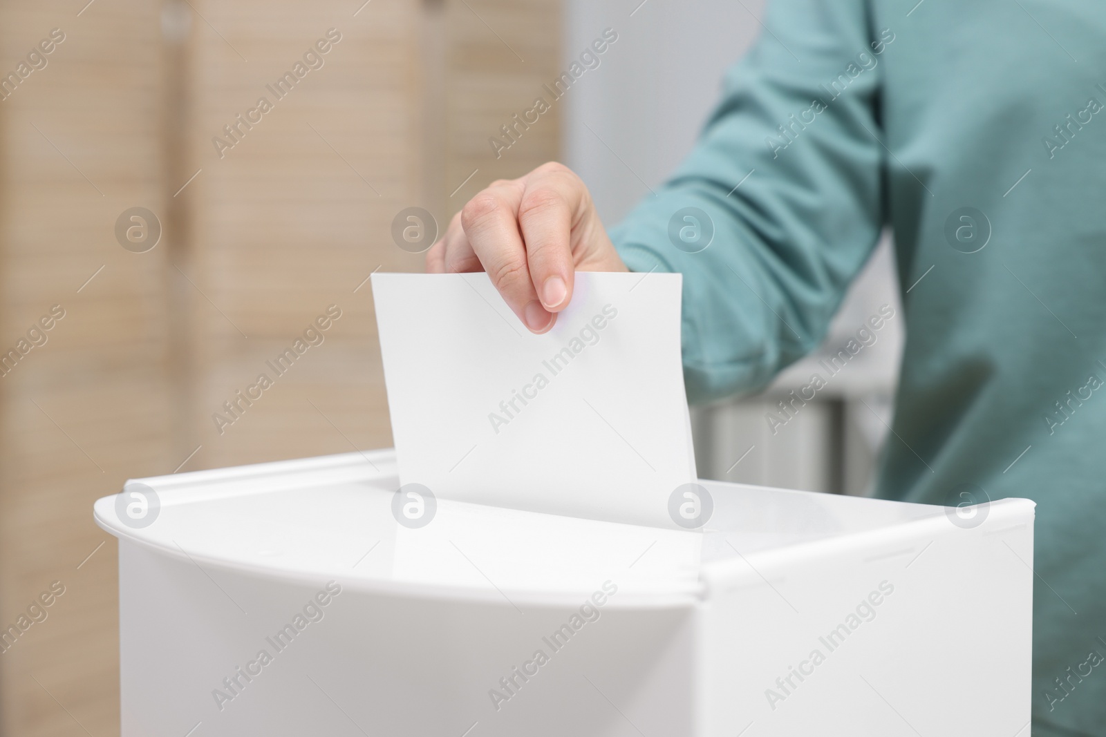 Photo of Woman putting her vote into ballot box on blurred background, closeup