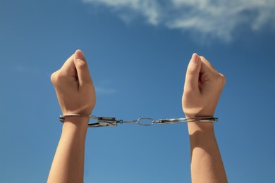 Photo of Woman in handcuffs against blue sky, closeup