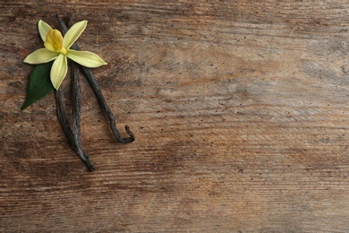 Photo of Flat lay composition with vanilla sticks and flower on wooden background. Space for text