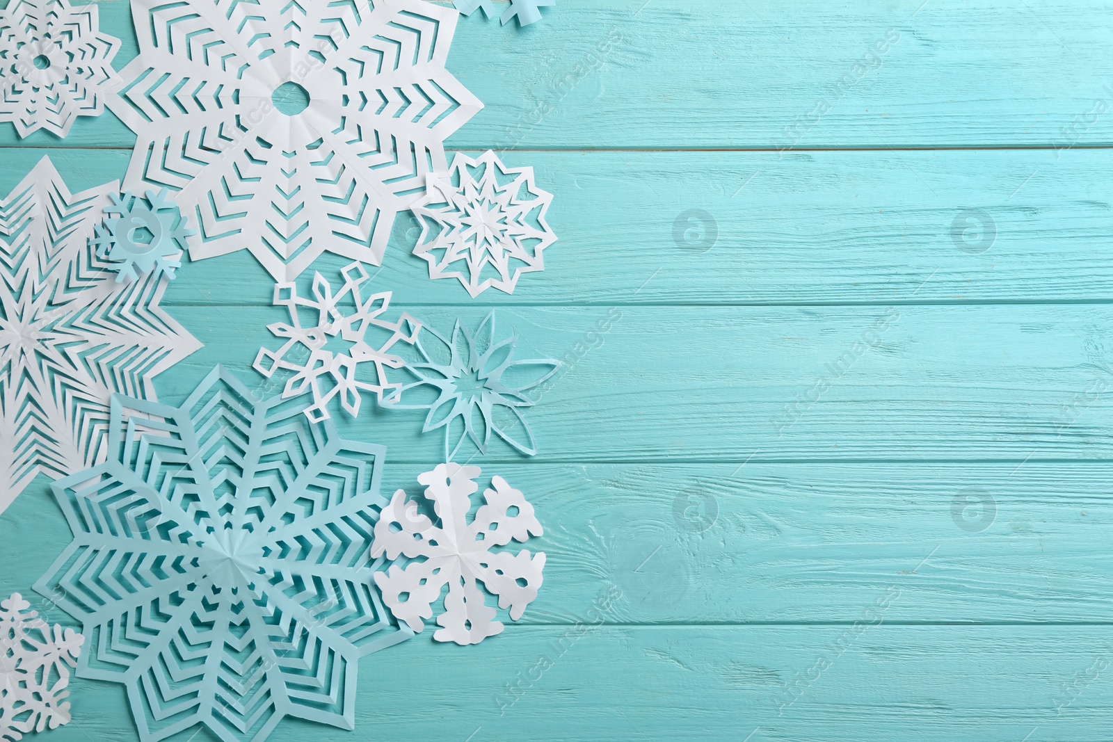 Photo of Many paper snowflakes on turquoise wooden background, flat lay. Space for text