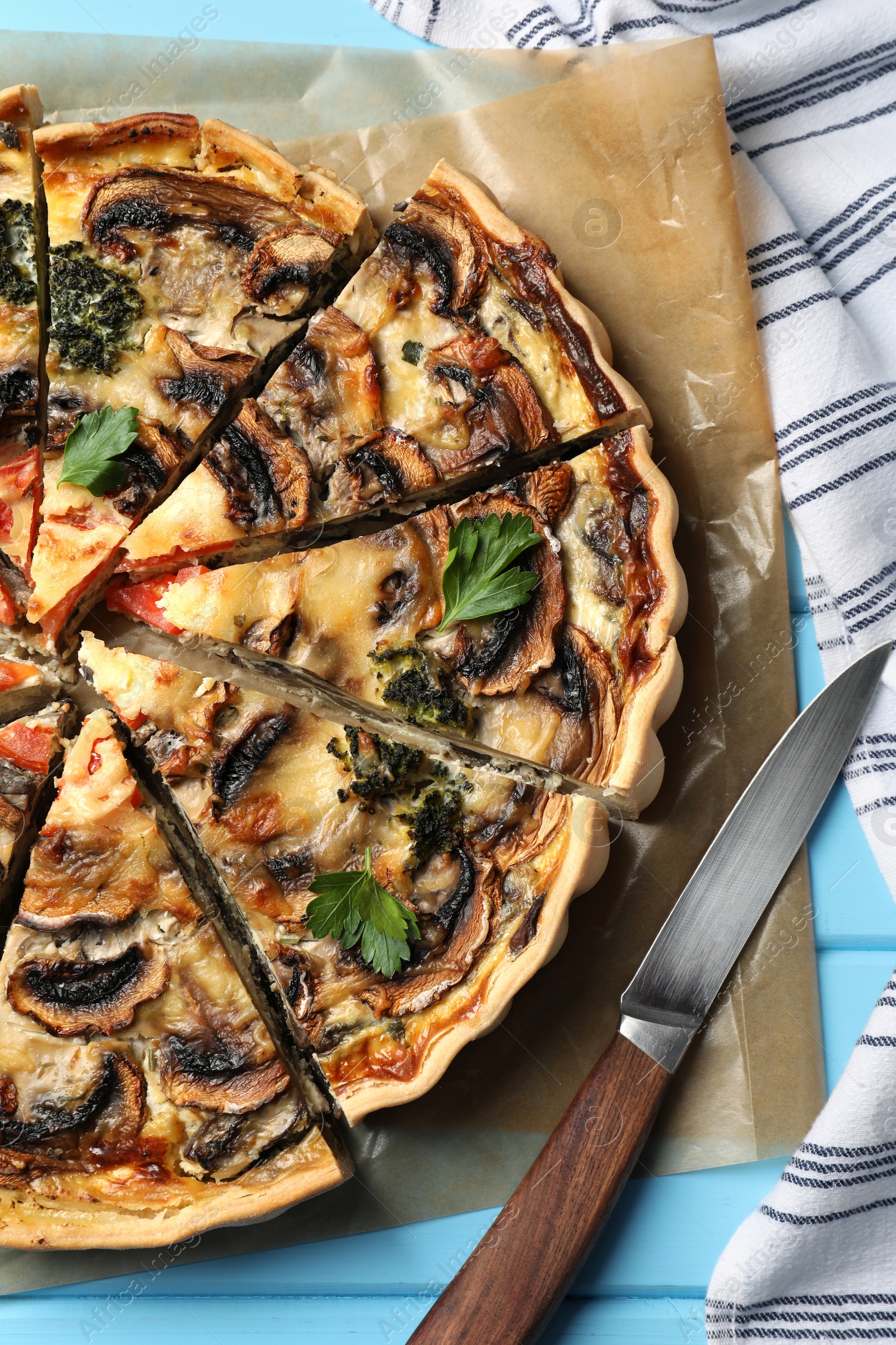 Photo of Delicious quiche with mushrooms and knife on light blue wooden table, flat lay