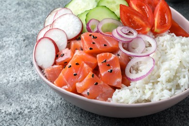 Delicious poke bowl with salmon and vegetables on grey table, closeup