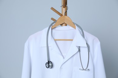 Photo of Medical uniform and stethoscope hanging on rack against light grey background