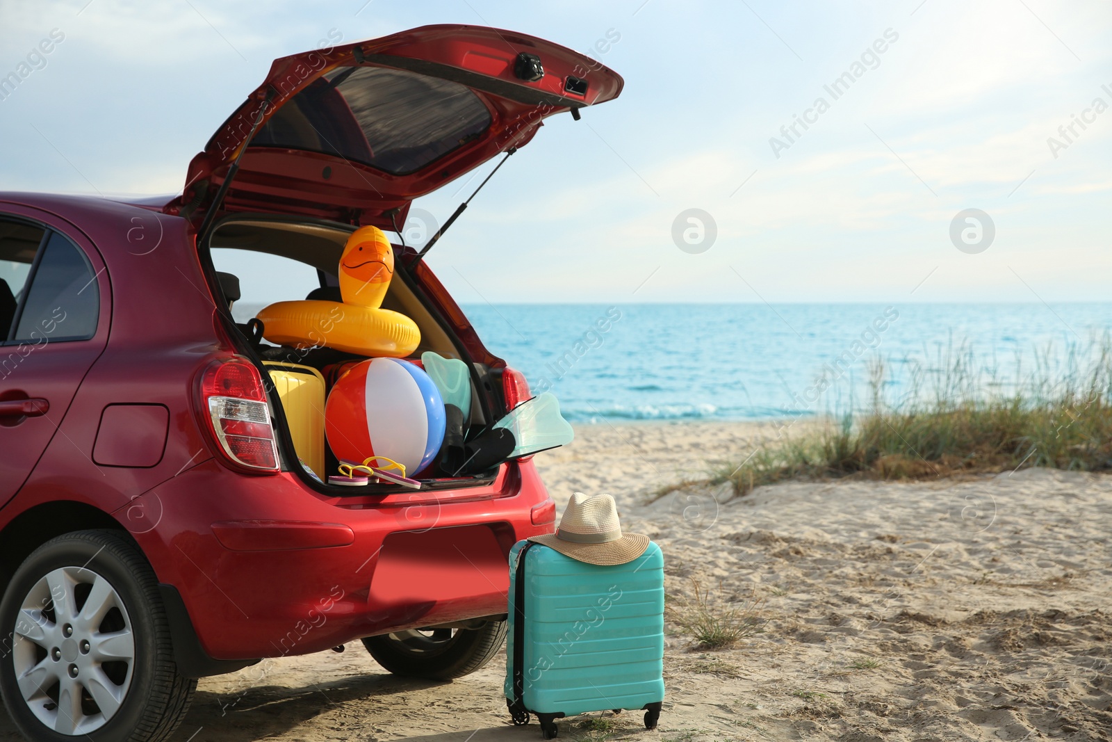 Photo of Red car luggage on beach, space for text. Summer vacation trip