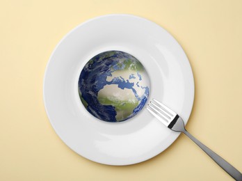 Image of Global food crisis concept. Globe of Earth in plate and fork on beige background, top view