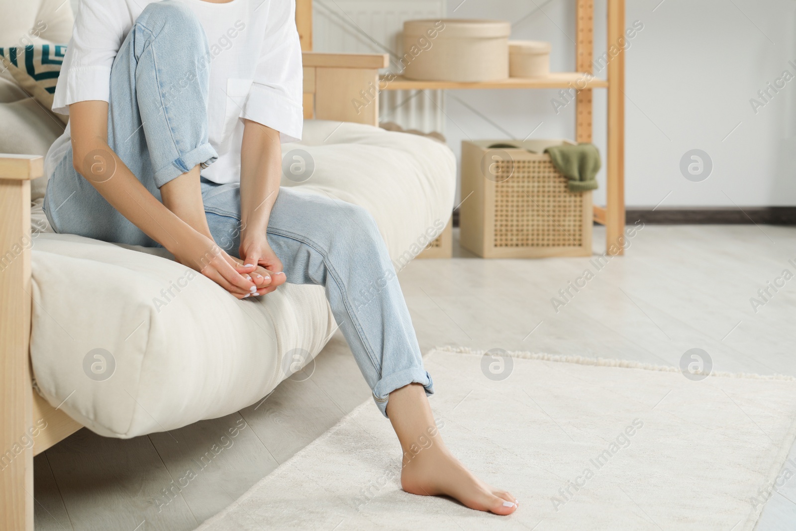 Photo of Woman rubbing sore foot on sofa at home, closeup. Space for text