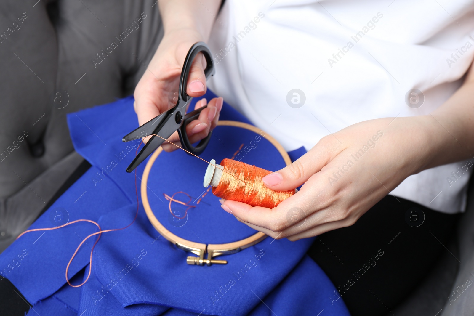 Photo of Woman cutting thread over embroidery hoop with cloth, closeup