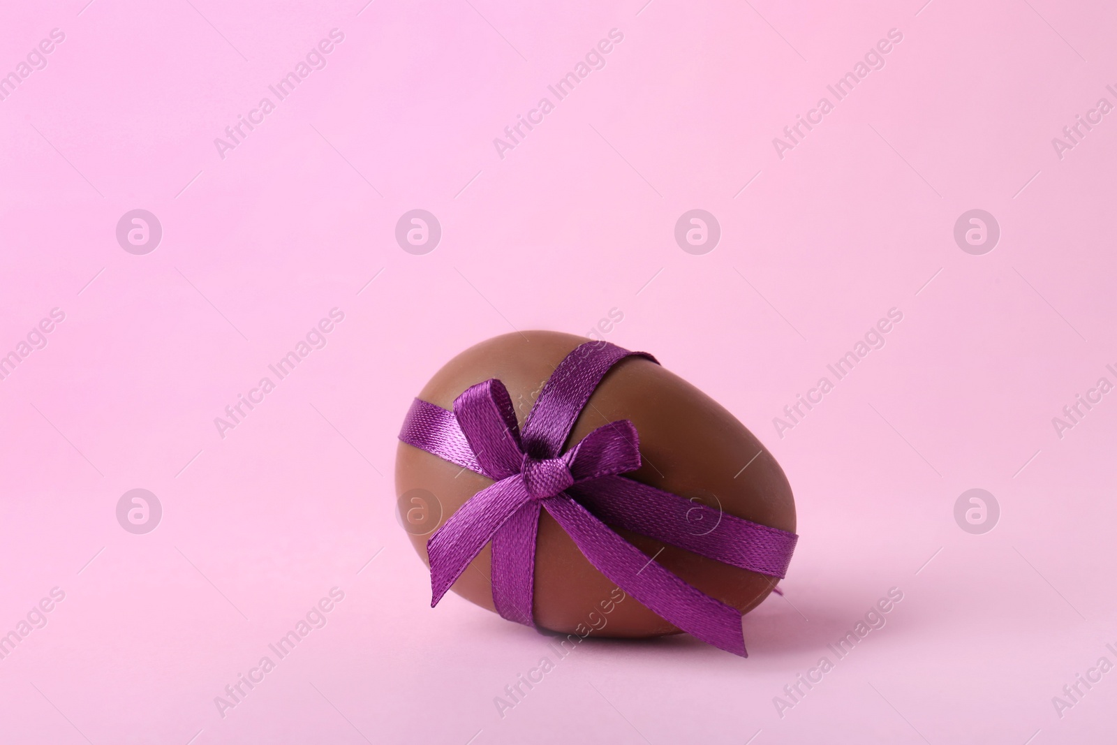 Photo of One tasty chocolate egg with purple bow on pink background