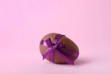 Photo of One tasty chocolate egg with purple bow on pink background
