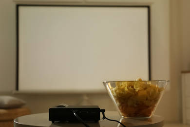 Video projector and bowl with chips on wooden table indoors