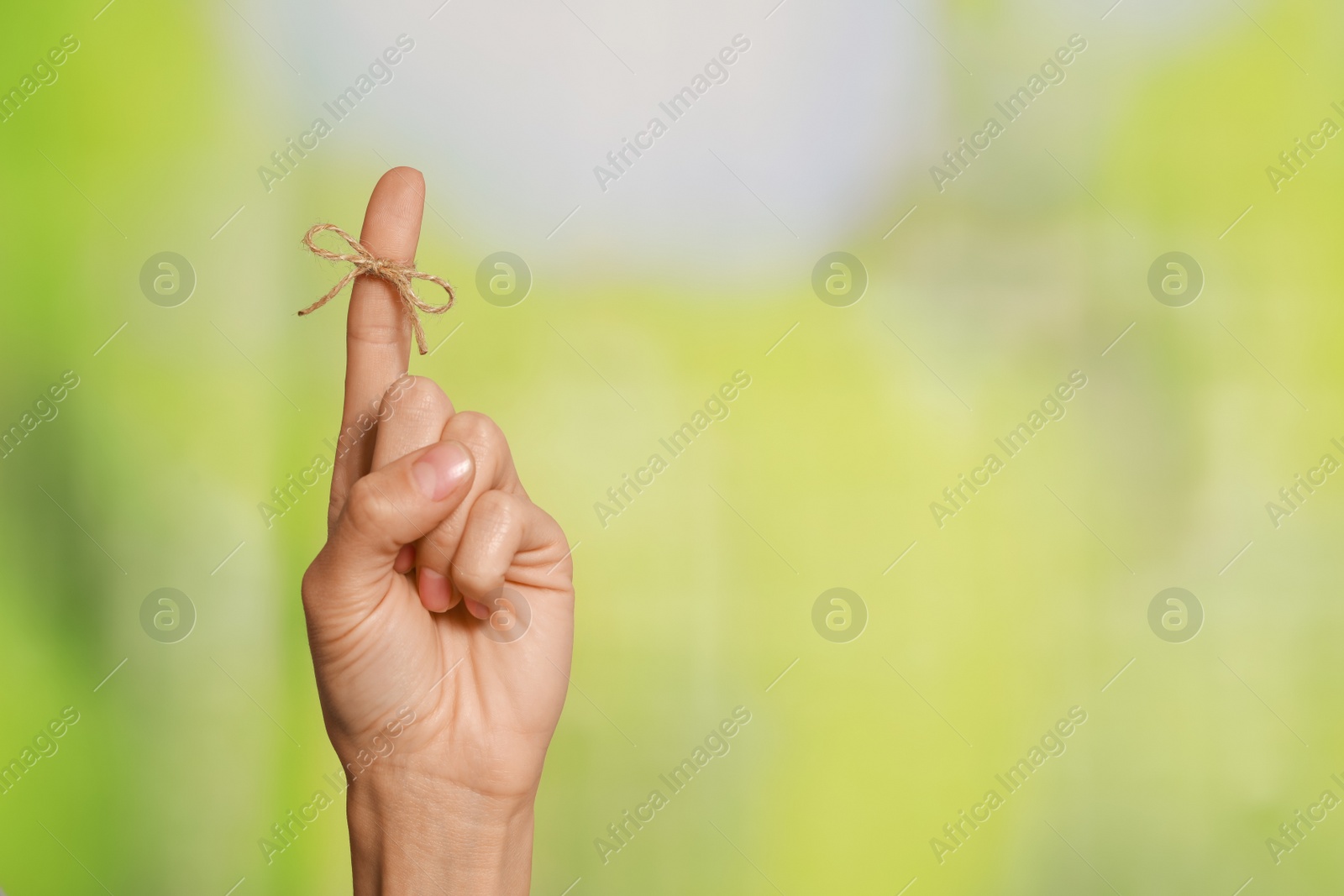 Photo of Woman showing index finger with tied bow as reminder on green blurred background, closeup. Space for text