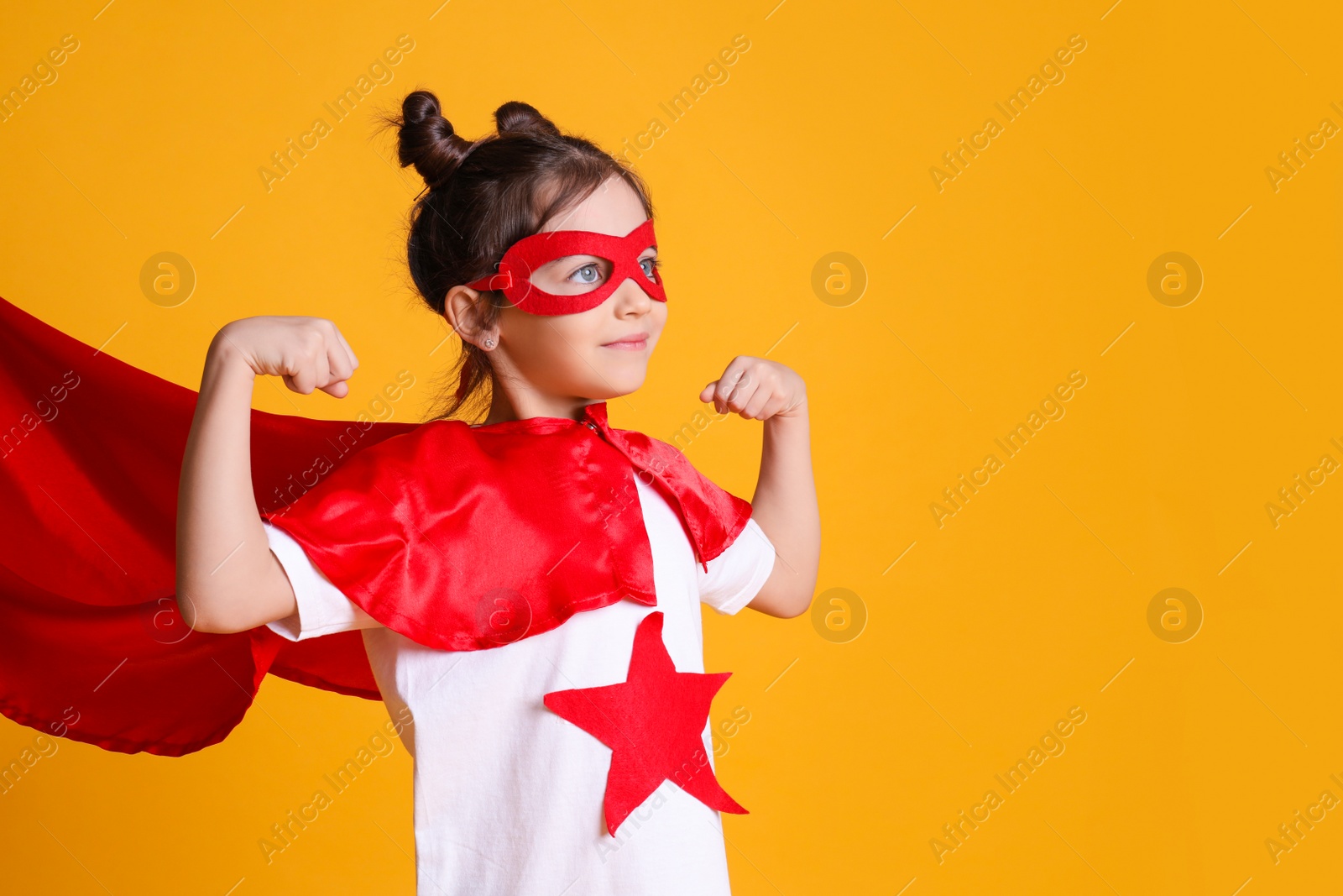 Photo of Cute little girl in superhero suit on yellow background. Space for text
