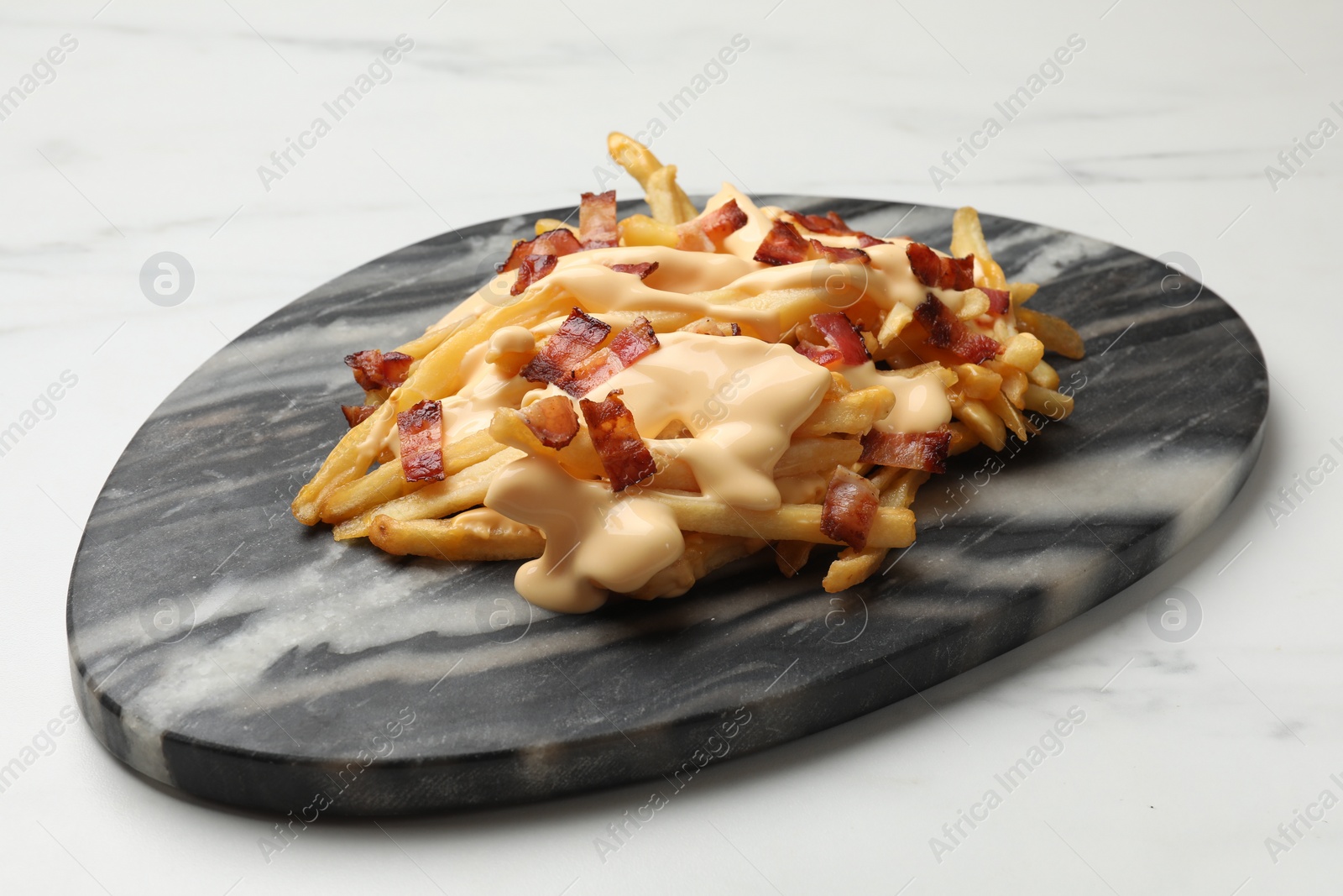 Photo of Delicious French fries with bacon and cheese sauce on white marble table, closeup