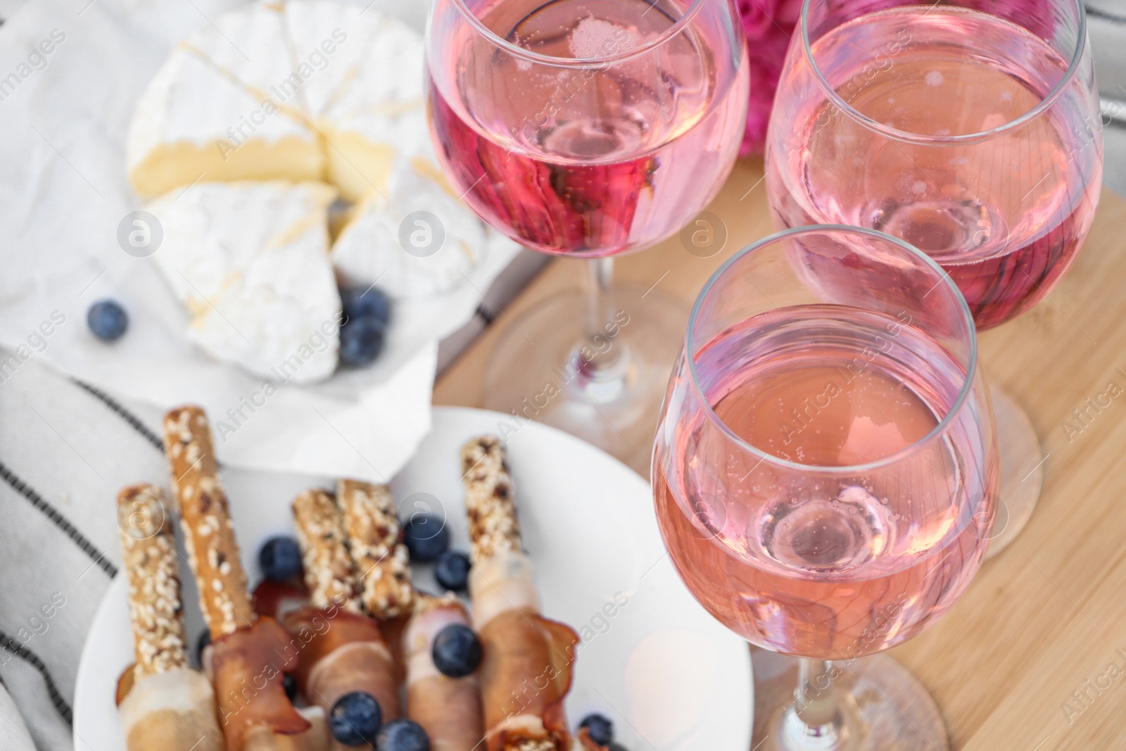 Photo of Glasses of delicious rose wine and food on white picnic blanket, closeup