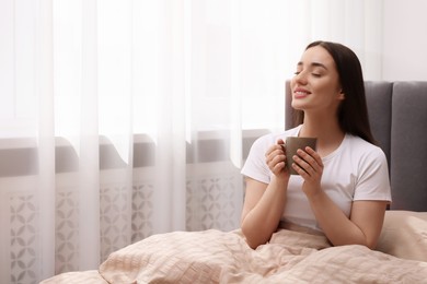Photo of Beautiful woman with cup of drink on bed at home, space for text. Lazy morning