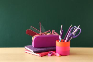 Photo of Different school stationery on wooden table near green chalkboard. Back to school