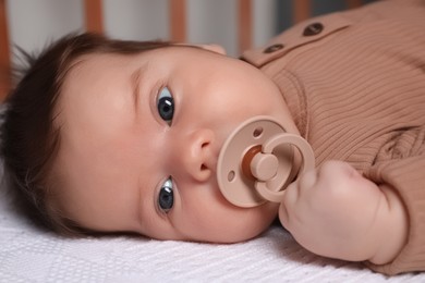 Photo of Cute little baby with pacifier lying in comfortable crib at home, closeup. Bedtime