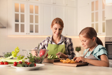 Photo of Mother and daughter cooking salad together in kitchen