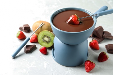 Photo of Dipping strawberry into fondue pot with chocolate on light marble table