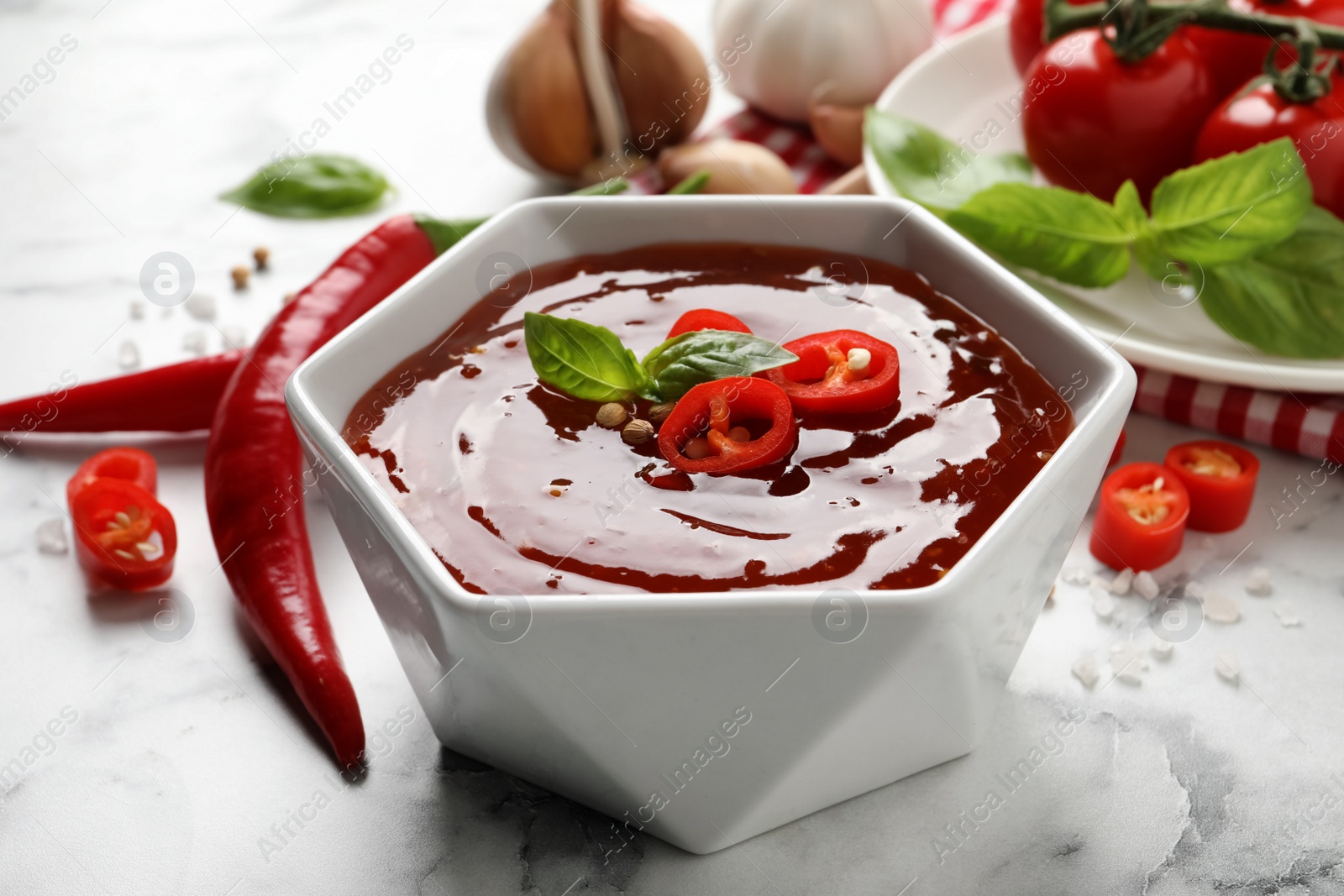 Photo of Spicy chili sauce with basil in bowl on white marble table