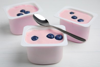 Photo of Plastic cups with tasty yogurts and blueberries on white wooden table