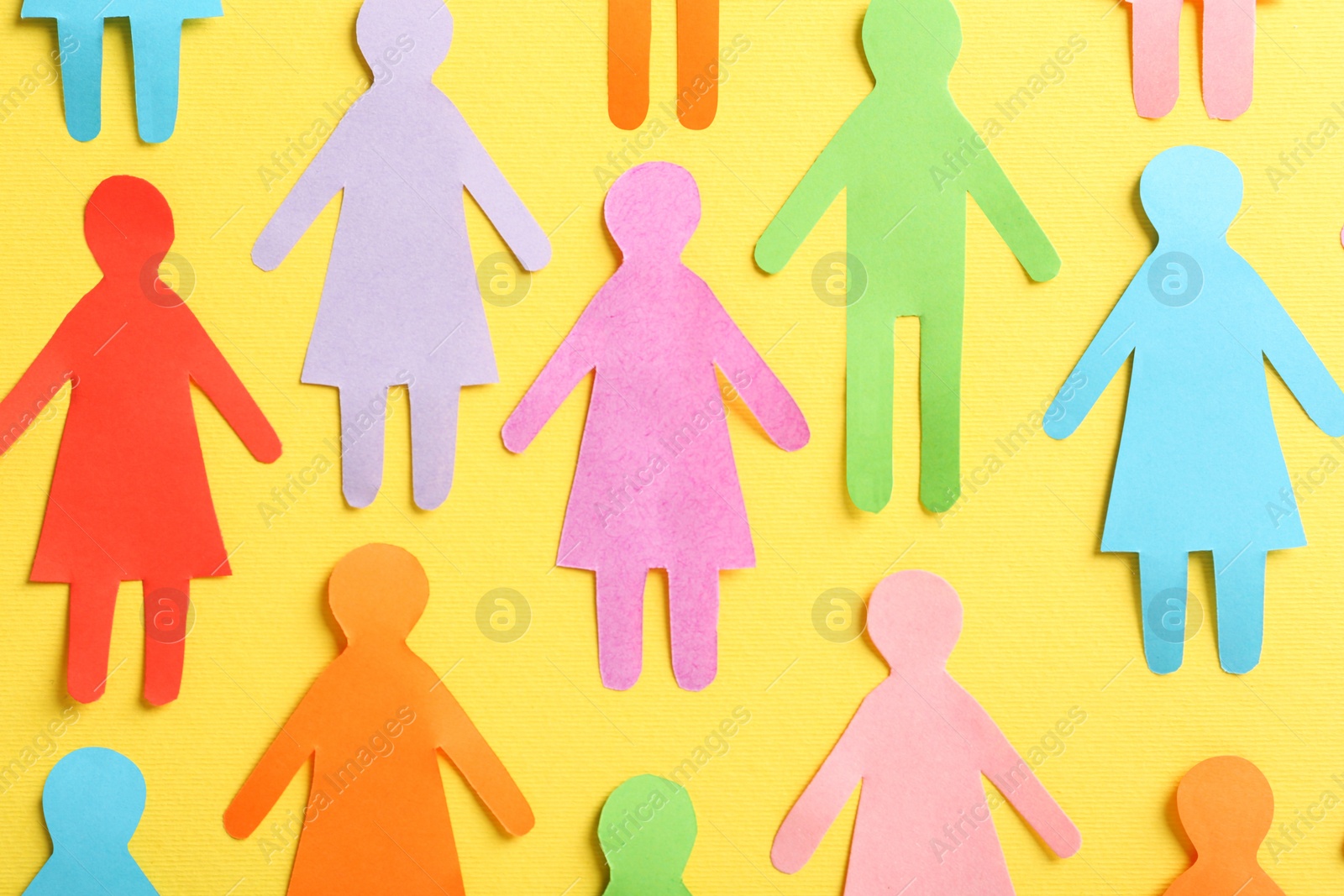 Photo of Many different paper human figures on yellow background, flat lay. Diversity and inclusion concept