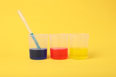 Photo of Beakers with colorful liquids on yellow background. Kids chemical experiment set