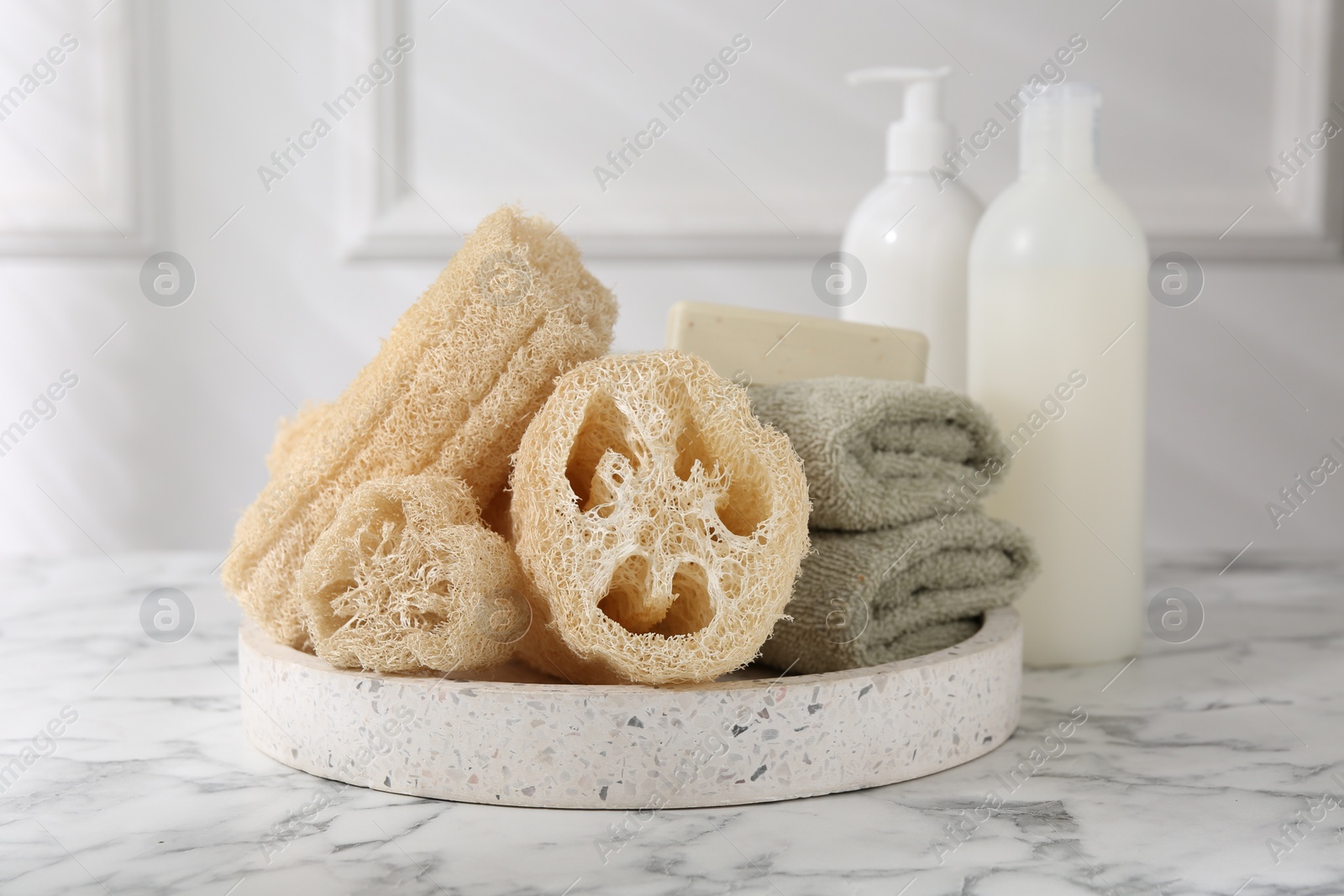 Photo of Loofah sponges, towels, soap and cosmetic products on white marble table