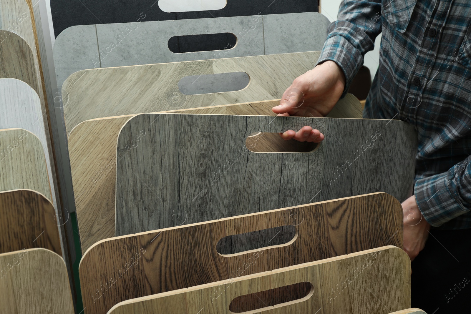 Photo of Man choosing wooden flooring among different samples in shop, closeup