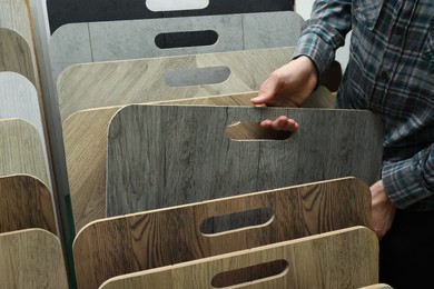 Man choosing wooden flooring among different samples in shop, closeup