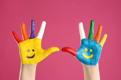 Kid with smiling faces drawn on palms against pink background, closeup