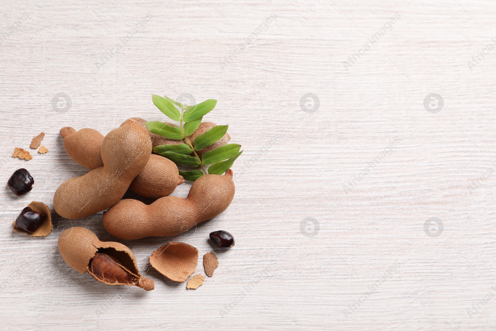 Photo of Delicious ripe tamarinds and leaves on white wooden table, flat lay. Space for text