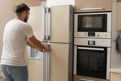 Photo of Young man opening refrigerator doors in kitchen