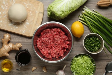 Photo of Bowl with minced meat, raw dough and ingredients for gyoza filling on wooden table, flat lay