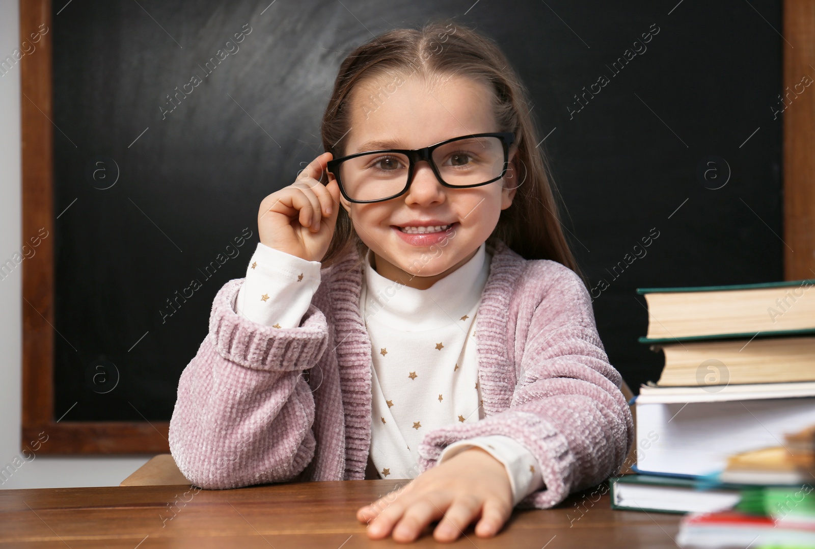 Photo of Cute little child wearing glasses at desk in classroom. First time at school