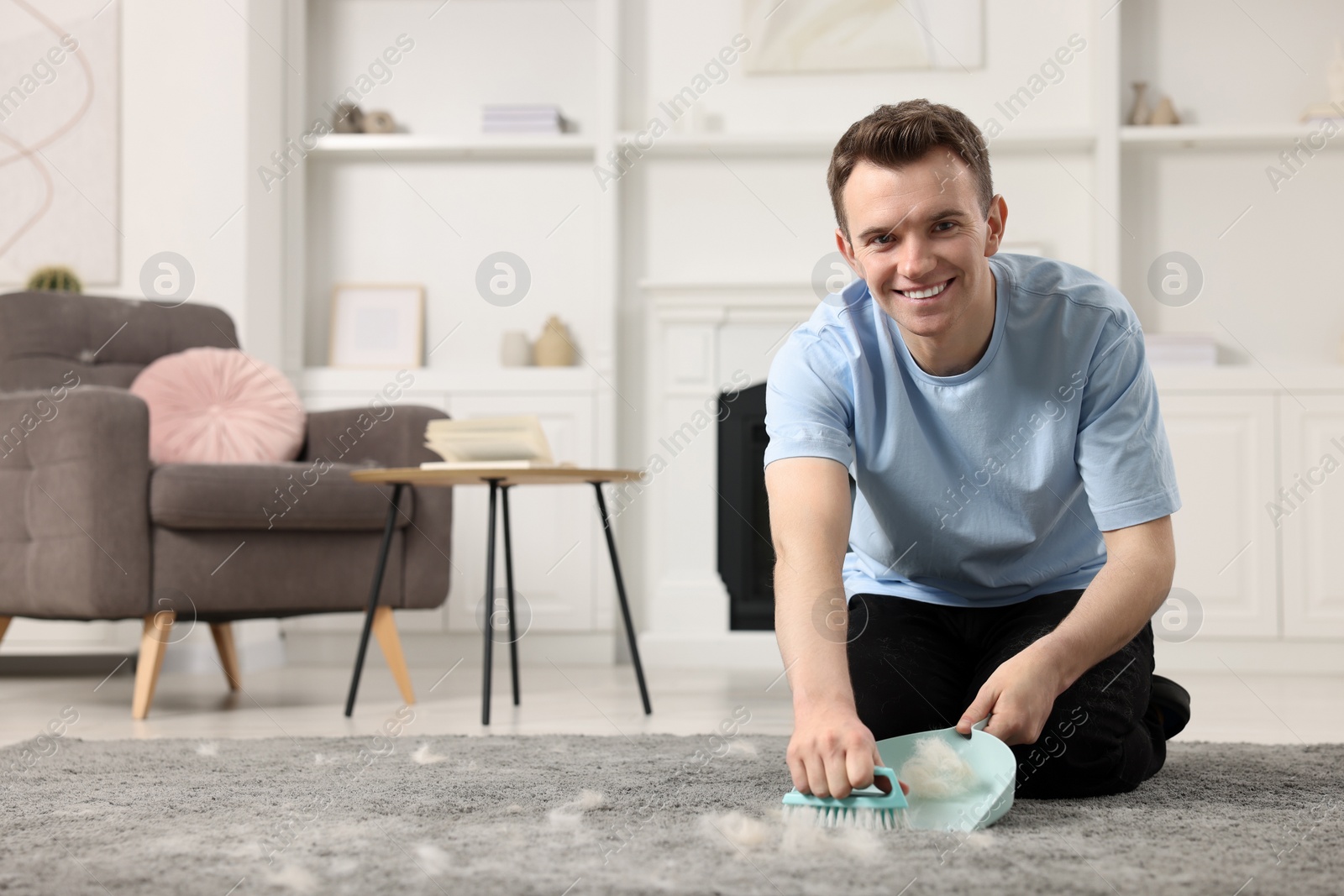 Photo of Smiling man with brush and pan removing pet hair from carpet at home. Space for text