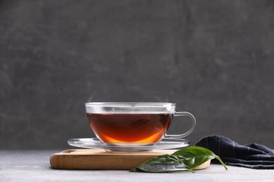 Aromatic hot tea in glass cup and leaves on light grey table
