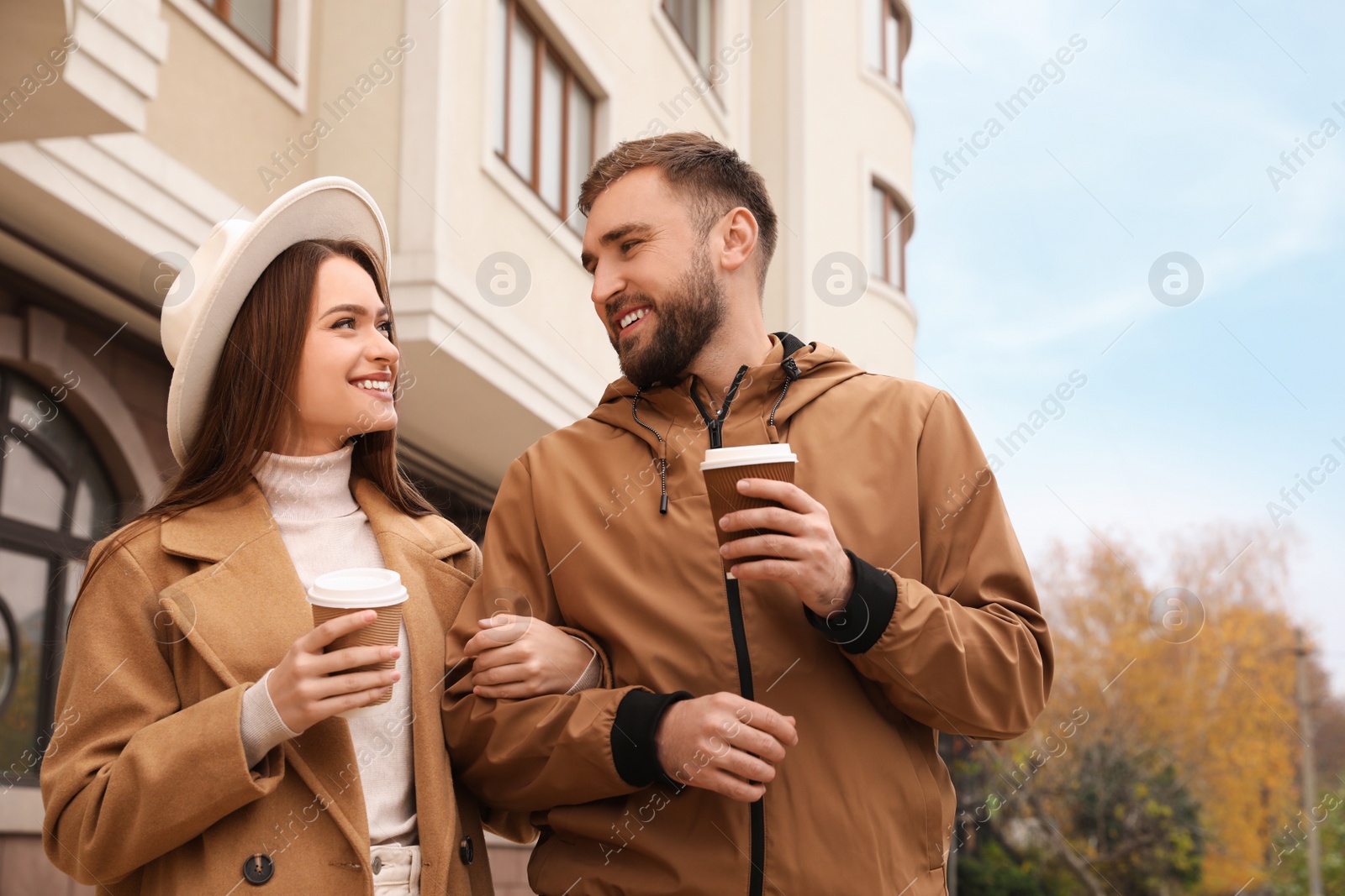 Photo of Happy couple wearing stylish autumn clothes with cups of coffee on city street