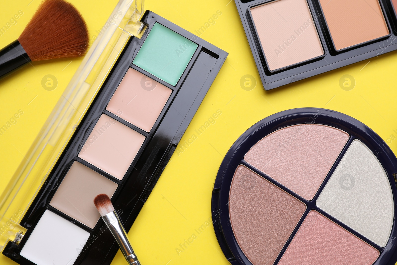 Photo of Different contouring palettes and brushes on yellow background, flat lay. Professional cosmetic product