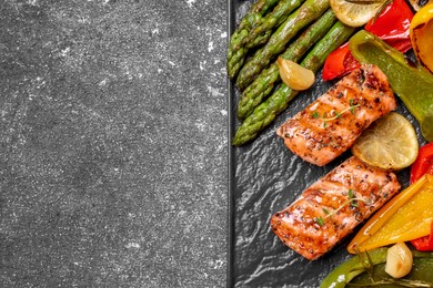 Tasty grilled salmon with lemon and vegetables on black table, top view. Space for text