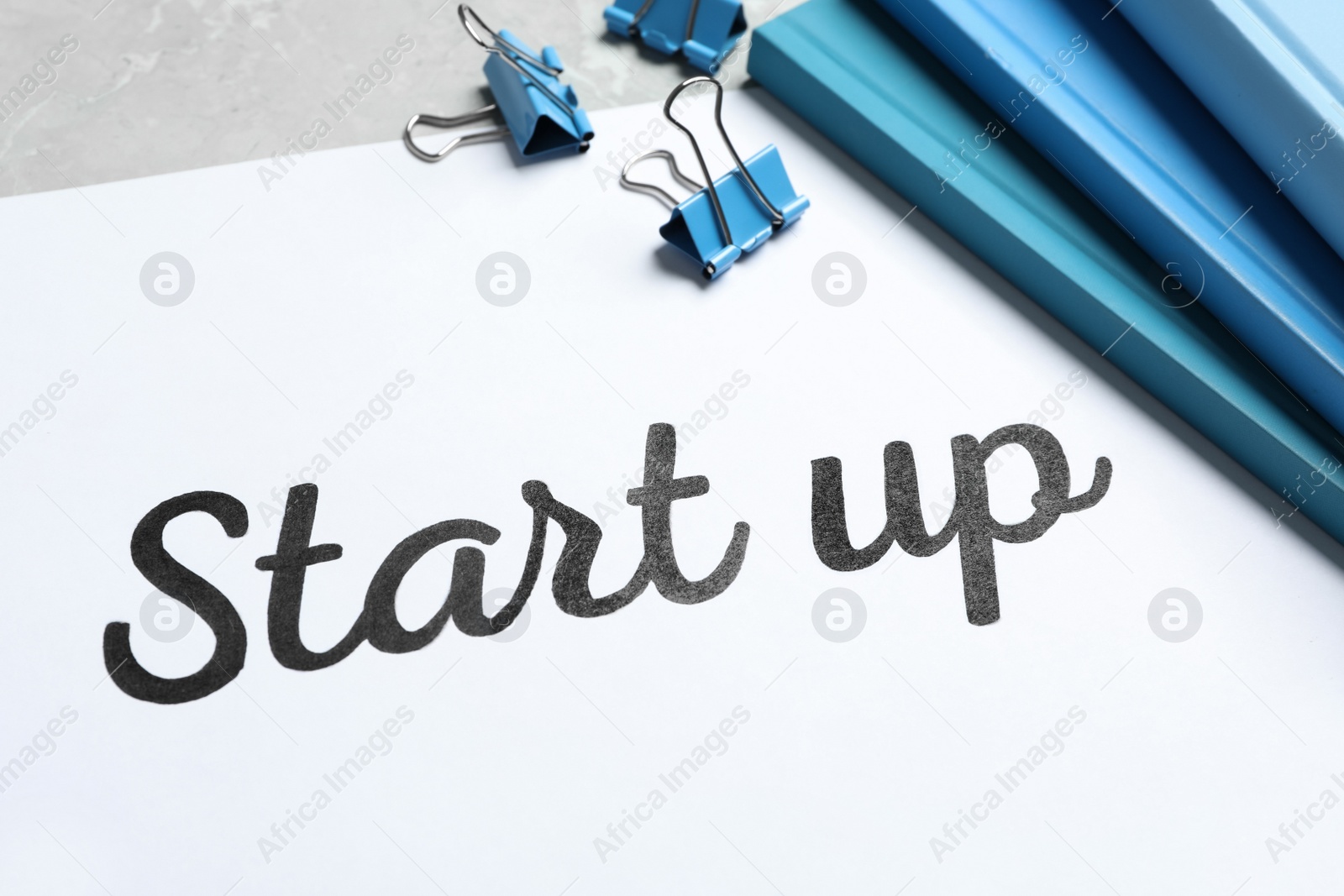 Photo of Sheet of paper with phrase Start Up and stationery on grey table, closeup