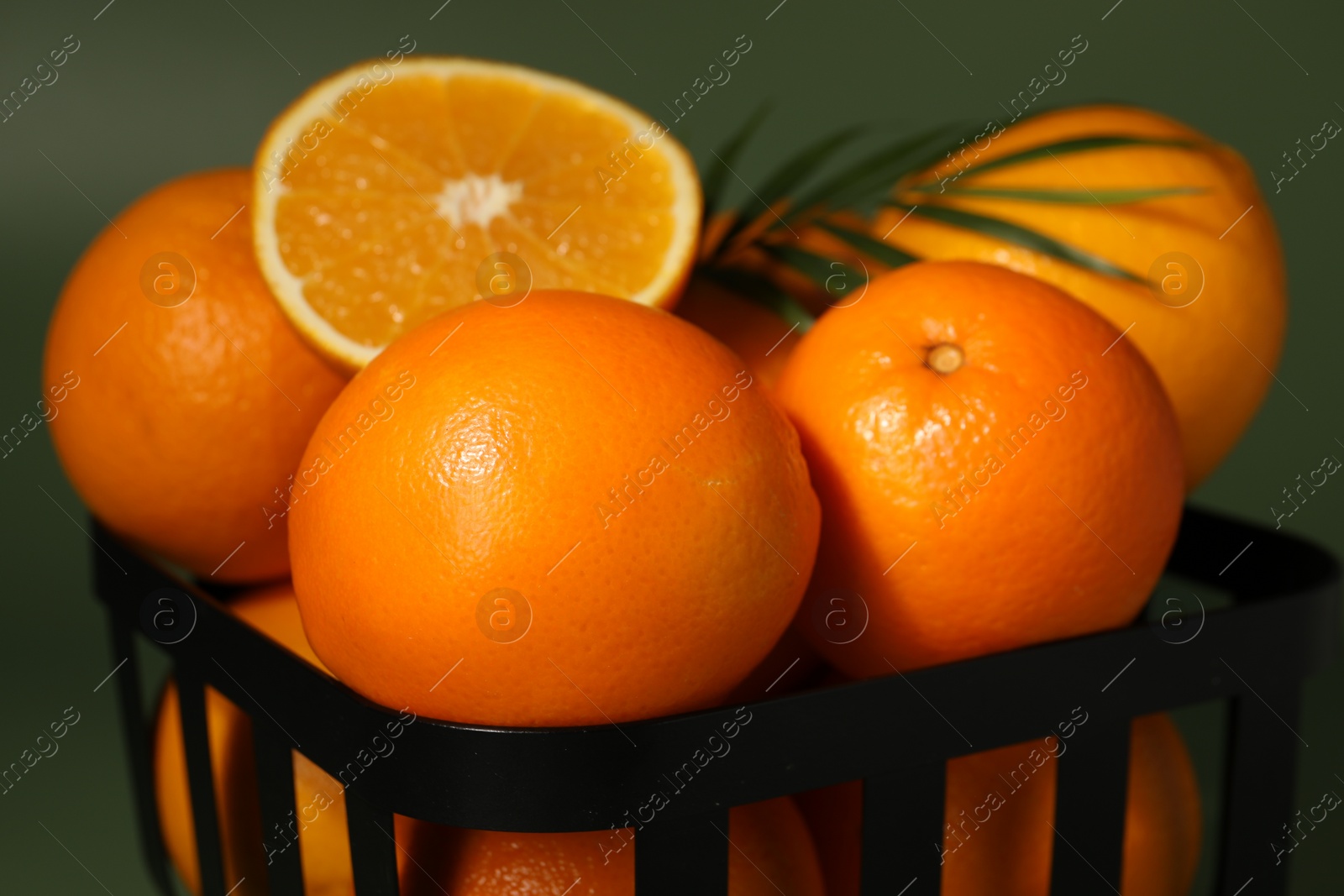 Photo of Fresh oranges in metal basket on green background, closeup