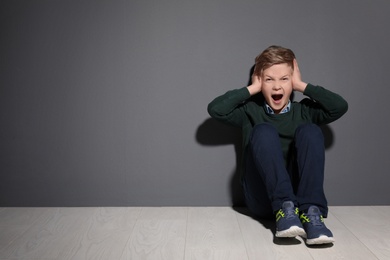 Photo of Depressed little boy sitting on floor indoors. Time to visit child psychologist