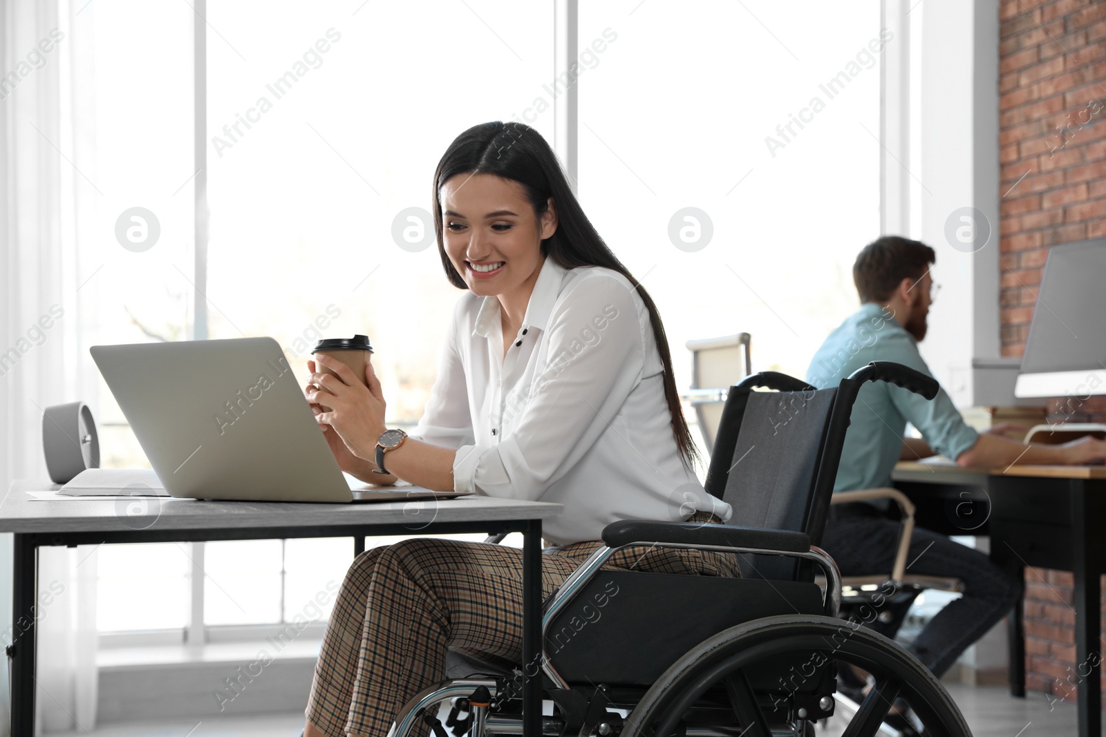 Photo of Young woman in wheelchair using laptop at workplace