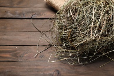 Burlap sack with dried hay on wooden table, closeup. Space for text